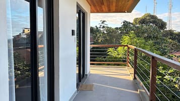 Un balcon abrité avec un plafond en bois, des portes vitrées et une vue sur les bâtiments et la végétation environnants.