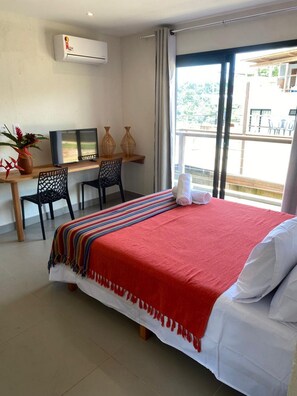 A hotel room with a bed, a desk with a computer, chairs, and a large window. - Villa Visgo Itacaré (Itacaré)