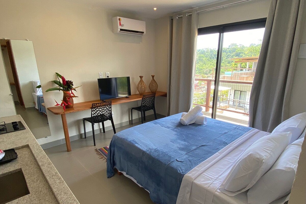 A hotel room with a bed, a desk with a computer, a TV, and a window with curtains.