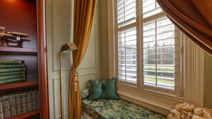 A cozy reading nook with a built-in bench, a bookshelf with books, and a window with blinds. - The Allen House (Ridgefield)