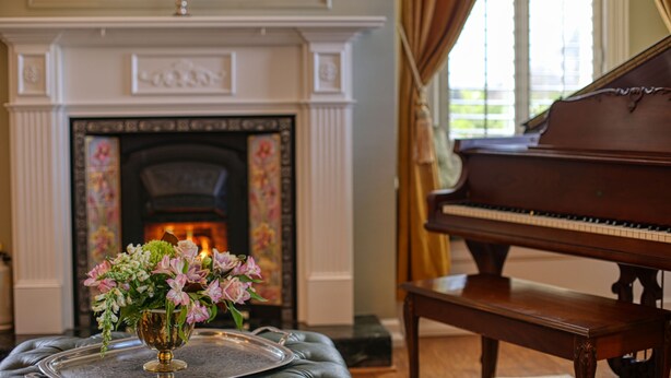 A grand piano, a fireplace with a decorative mantel, and a vase of flowers on a table. - The Allen House (Ridgefield)