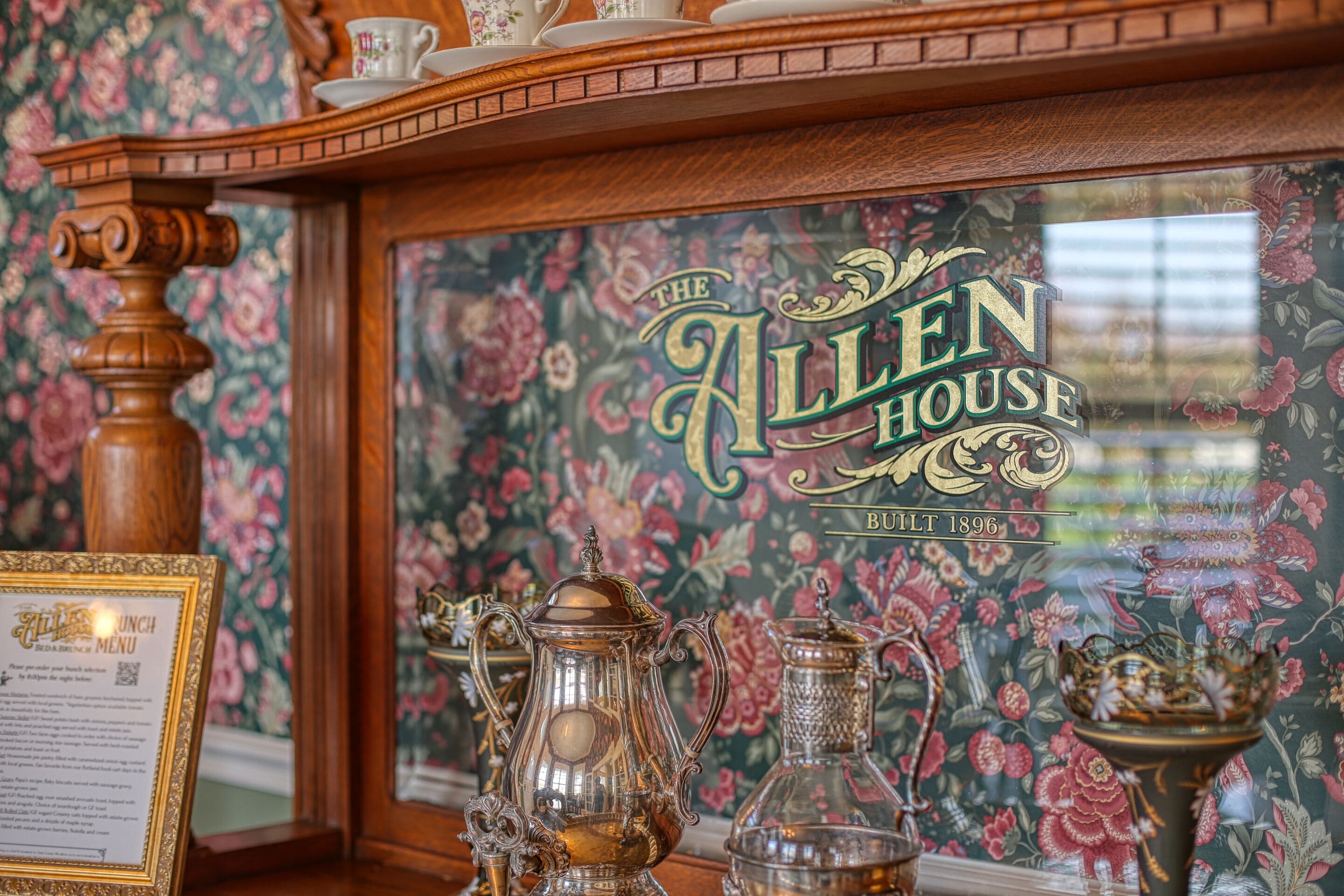A vintage interior with ornate furniture, a framed menu, and a floral wallpaper backdrop.