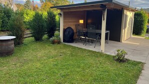 A covered patio area with a table and chairs, a barbecue grill, and a small shed.