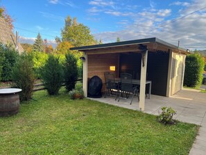 Un patio couvert avec une table et des chaises, un barbecue et un petit abri de jardin.