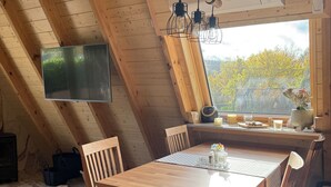 En matplats med träinredning, bestående av ett bord och stolar, en hängande lampa och ett fönster med utsikt över träd.