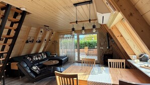 Ett mysigt rum inrett i vindslägenhetsstil med ett träpanelat tak, en svart lädersoffa, ett matbord med stolar och en trappa.