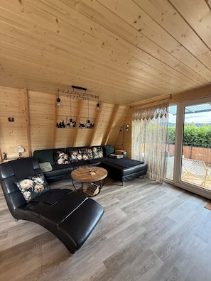 A cozy living room with a sectional sofa, a round coffee table, and a large sliding glass door to the outdoors.