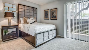 Quarto com cabeceira estofada, mesa de cabeceira com abajur e duas fotos emolduradas na parede.