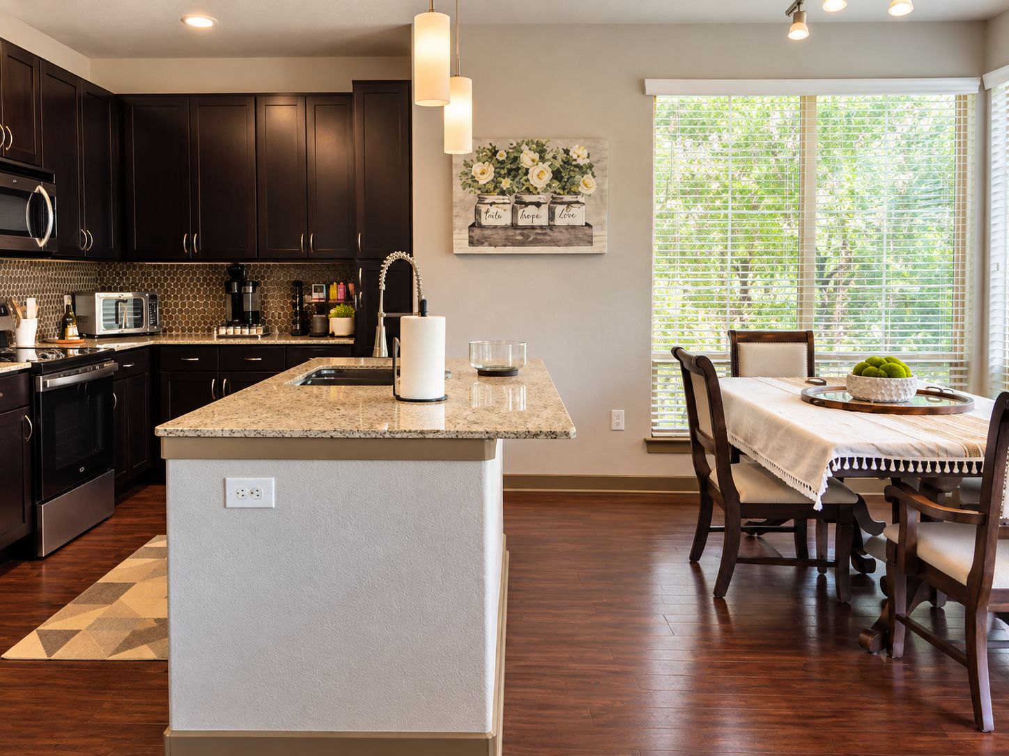 A modern kitchen with dark cabinets, a granite countertop, and a dining area with a table and chairs.