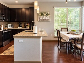 A modern kitchen with dark cabinets, a granite countertop, and a dining area with a table and chairs. -  2BR Corporate Stay Near UT Southwestern & Love Field (Dallas)