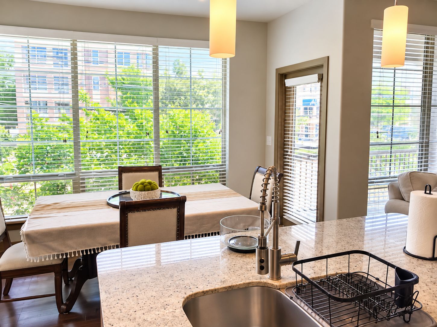 A modern kitchen with a granite countertop, stainless steel sink, and a dining area with a bench and chairs.