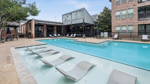 Uma piscina com espreguiçadeiras e um edifício com grandes janelas ao fundo.