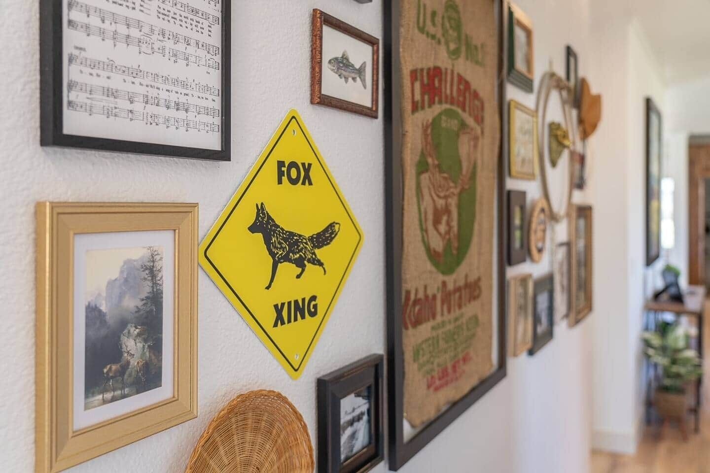 A wall with various framed items including a yellow sign with a fox silhouette, a framed musical score, and several other framed pictures and posters.