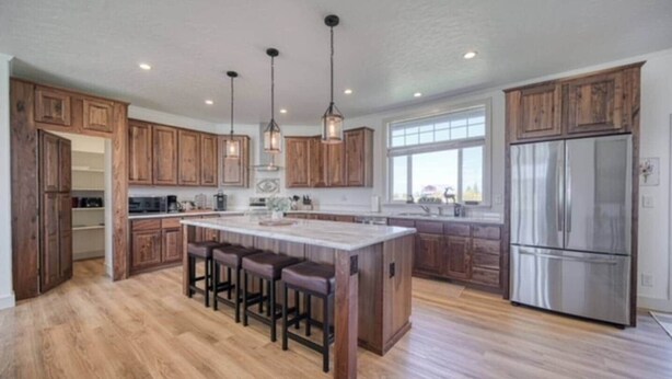 Una cocina amplia con armarios de madera, una isla central con taburetes de bar, un refrigerador de acero inoxidable e iluminación colgante.