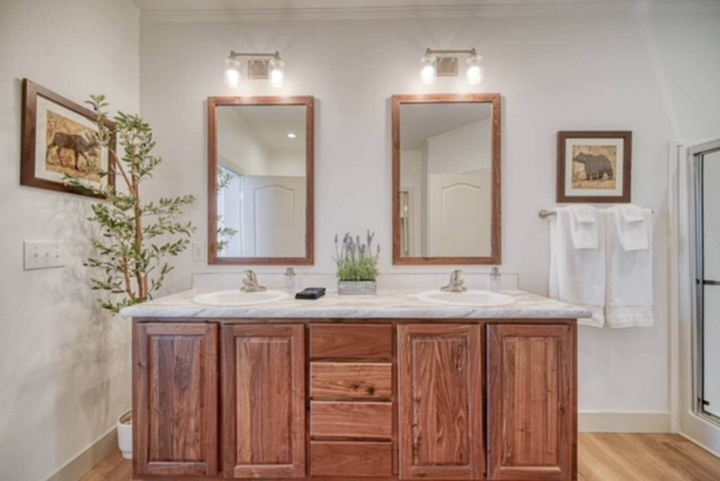 Un baño con tocador doble, armarios de madera, dos espejos y una planta en maceta.