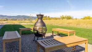 Un patio con un farol de metal, dos mesas de madera y un campo cubierto de hierba con montañas al fondo.