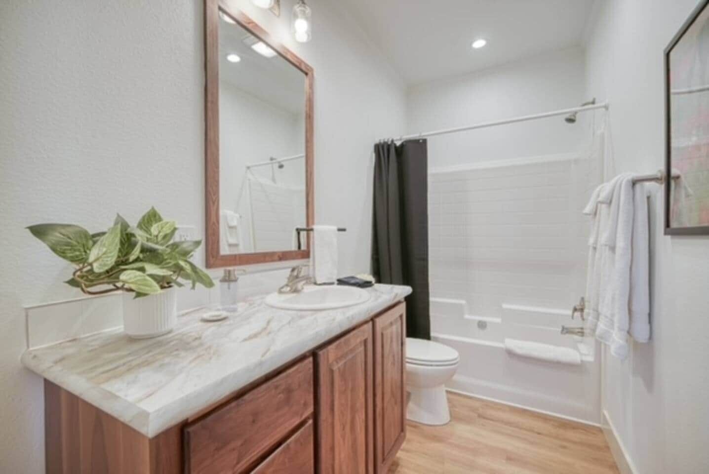 A bathroom with a marble vanity, a toilet, a shower, and a large mirror.