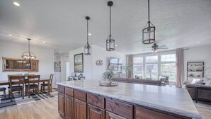 Una cocina amplia con una isla grande, armarios de madera, iluminación colgante y un comedor con mesa y sillas.