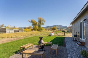 Un patio con una griglia, un vaso grande e un set tavolo e sedie in legno.
