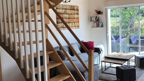 A wooden staircase leading to a living area with a grey sofa, a coffee table, and a view of the outdoors through large windows. - Charming cottage (Monteux)