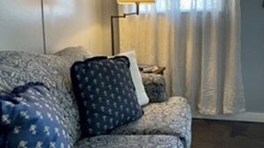 A room with a patterned sofa, a lamp, and a window with curtains. - Charming 1BR Pet-Friendly Cottage - Peaceful Stay Near Downtown New Albany (New Albany)