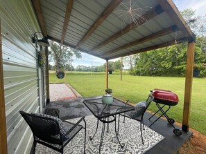 An outdoor patio with a covered seating area, a grill, and a potted plant.