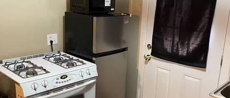 A compact kitchen with a gas stove, a refrigerator, and a microwave.