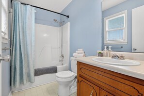 A bathroom with a shower, toilet, and sink, featuring a blue wall and wooden vanity. - Eagles Rest Home • Sleeps 7 • Minutes to Army Base (Oak Grove)