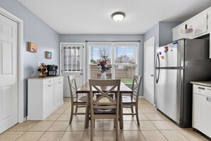 A kitchen with a dining table, chairs, a refrigerator, and a window with blinds. - Eagles Rest Home • Sleeps 7 • Minutes to Army Base (Oak Grove)