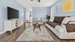 Ein Wohnzimmer mit Flachbildfernseher, Deckenventilator, Sofa und Couchtisch.