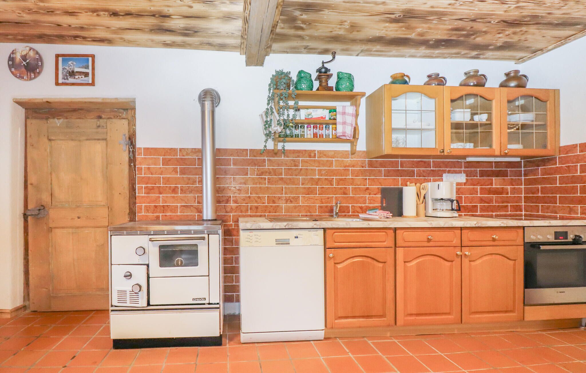 A kitchen with a stove, dishwasher, wooden cabinets, and a brick backsplash.