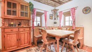 Une salle à manger rustique avec une table et des chaises en bois, un buffet aux portes vitrées et des rideaux à carreaux.