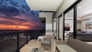 A balcony with wicker furniture, a glass railing, and a sunset view. - 3 bedroom high end beach front condo with amazing view (Mazatlán)