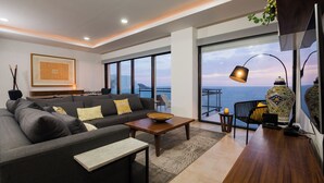 A modern living room with a sofa, coffee table, and a view of the sea through large windows. - 3 bedroom high end beach front condo with amazing view (Mazatlán)