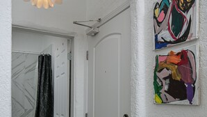 Un couloir avec une porte blanche, un espace douche et une table en bois.