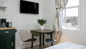 Une petite pièce avec un téléviseur fixé au mur, une table avec deux chaises, une machine à café et une plante.