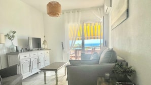Ein Wohnzimmer mit einer Couch, einem kleinen Tisch, einem Fernseher und einem Fenster mit Vorhängen.