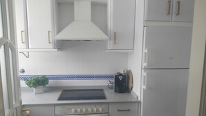 Eine kleine Küche mit weißen Schränken, einem Einbauofen, einem Herd und einer Arbeitsplatte mit Toaster und Pflanze.