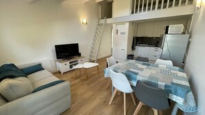 A compact living space with a sofa, a TV, a dining table with chairs, a kitchen area, and a loft bedroom. - Vent de Mer - House with a pool for 8 people (Bretignolles-sur-Mer)