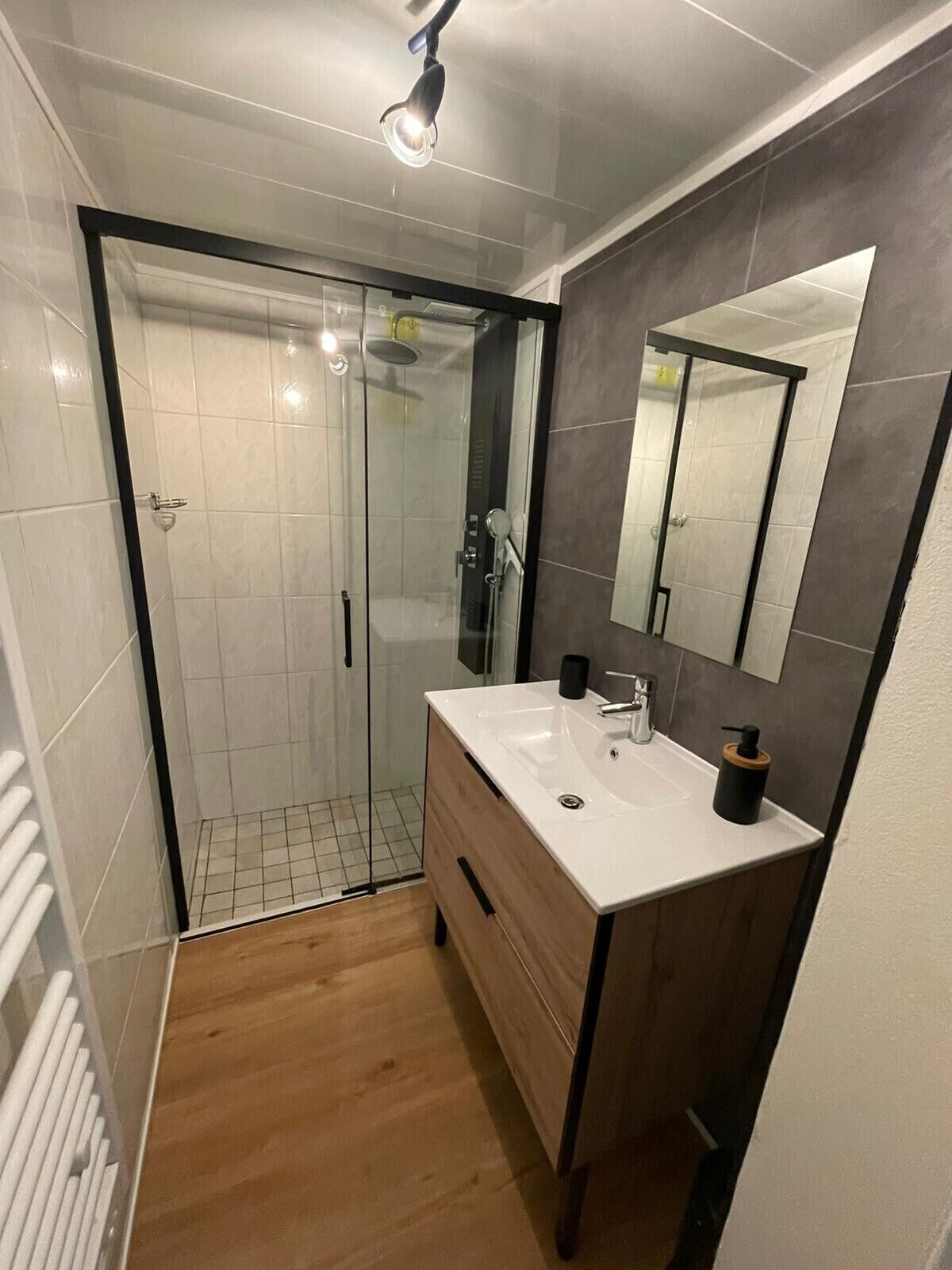 A modern bathroom with a glass-enclosed shower, a white sink with a mirror, and wooden cabinetry.