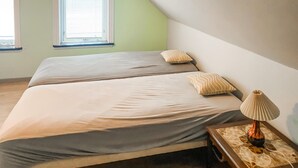 Ein Schlafzimmer mit zwei Betten, einem Nachttisch mit Lampe und einem Fenster mit Jalousien.