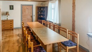 Ein Esszimmer mit einem langen Holztisch und passenden Stühlen, einem Holzschrank und einem Fenster mit Vorhängen.