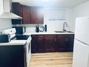 A compact kitchen with dark wooden cabinets, a white countertop, a built-in microwave, a coffee maker, and a refrigerator. - Amazing Location, Blocks from UW (Seattle)