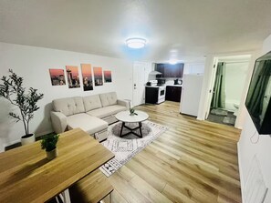 A modern living room with a sofa, coffee table, and a dining area with a wooden table. A kitchen is visible in the background with a microwave and stove. - Amazing Location, Blocks from UW (Seattle)