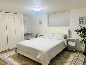 A bedroom with a bed, bedside tables, a desk, and a chair. There are two doors, a window with blinds, and wall art. - Amazing Location, Blocks from UW (Seattle)