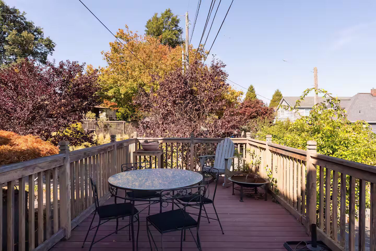 Une terrasse en bois avec une table ronde et des chaises, entourée d’une balustrade en bois.