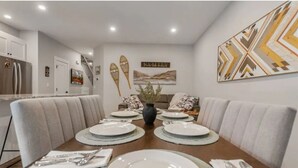 A dining area with a long table set for four, surrounded by cushioned booths, a vase centerpiece, and wall art. - Apex Slopeside Escape ~ Ski in/out with Hot tub (Keremeos)
