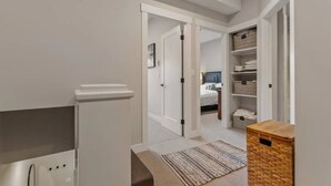 A narrow hallway with a white door leading to a bedroom. A wooden chest of drawers is visible on the right, and a patterned rug is on the floor. - Apex Slopeside Escape ~ Ski in/out with Hot tub (Keremeos)