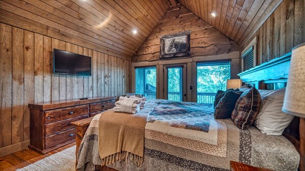 Un dormitorio acogedor con paredes de madera, una cama grande con colcha, un aparador y un televisor montado.