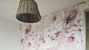 A bedroom with a floral wallpaper, a bed with pink bedding, striped pillows, and a woven light fixture.